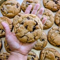 A hand holding a big cookie over a tray of cookies