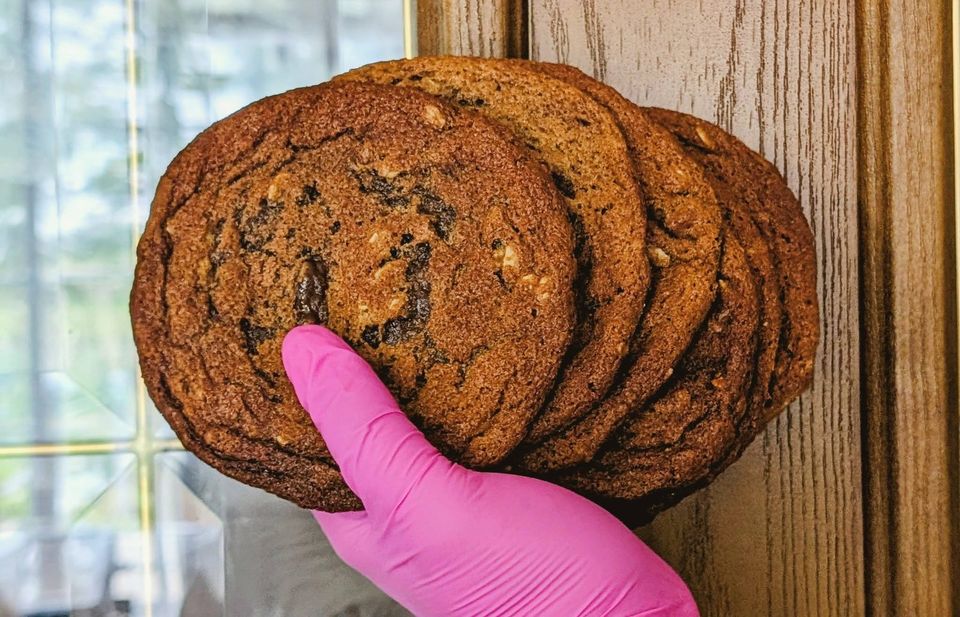A pink-gloved hand holding a stack of big cookies