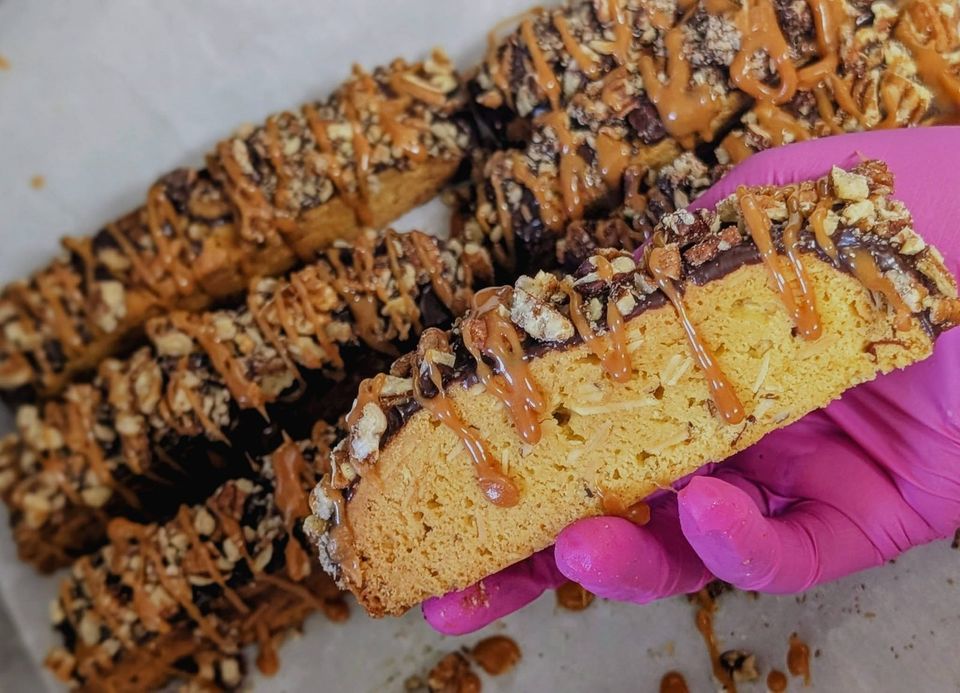 A pink-gloved hand holding a drizzled cookie bar
